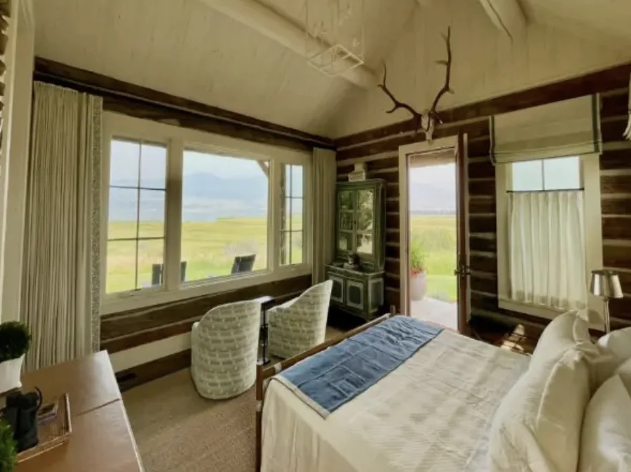 Log-walled primary suite with mountain views, linen drapery, and patterned swivel chairs